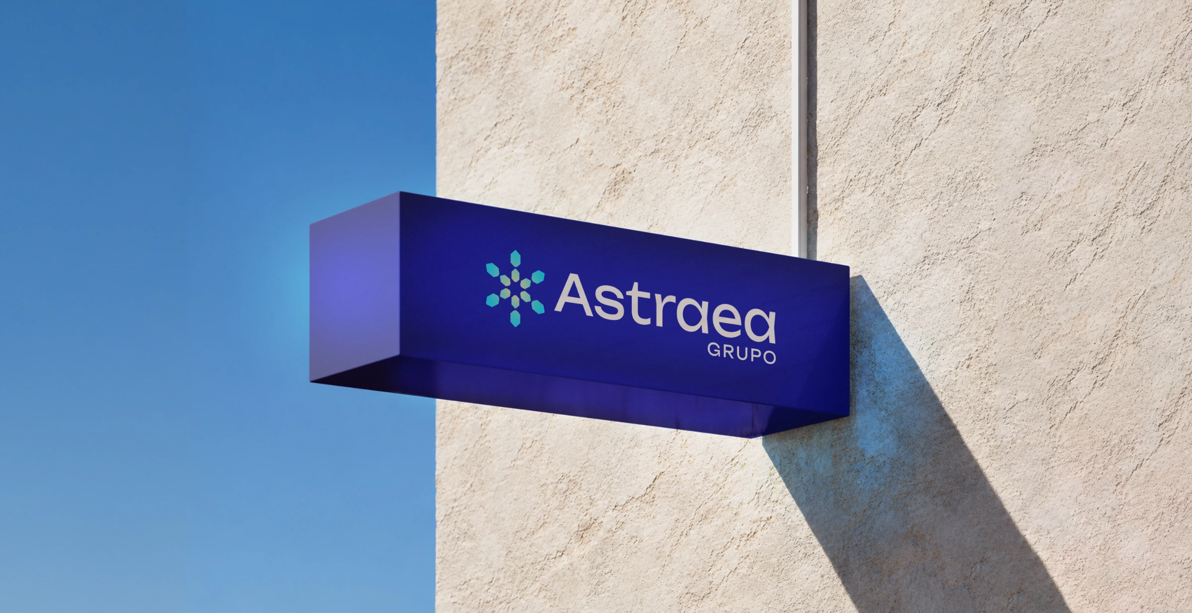 Letrero corpóreo azul con el logotipo de Astraea Grupo en una fachada beige bajo un cielo azul