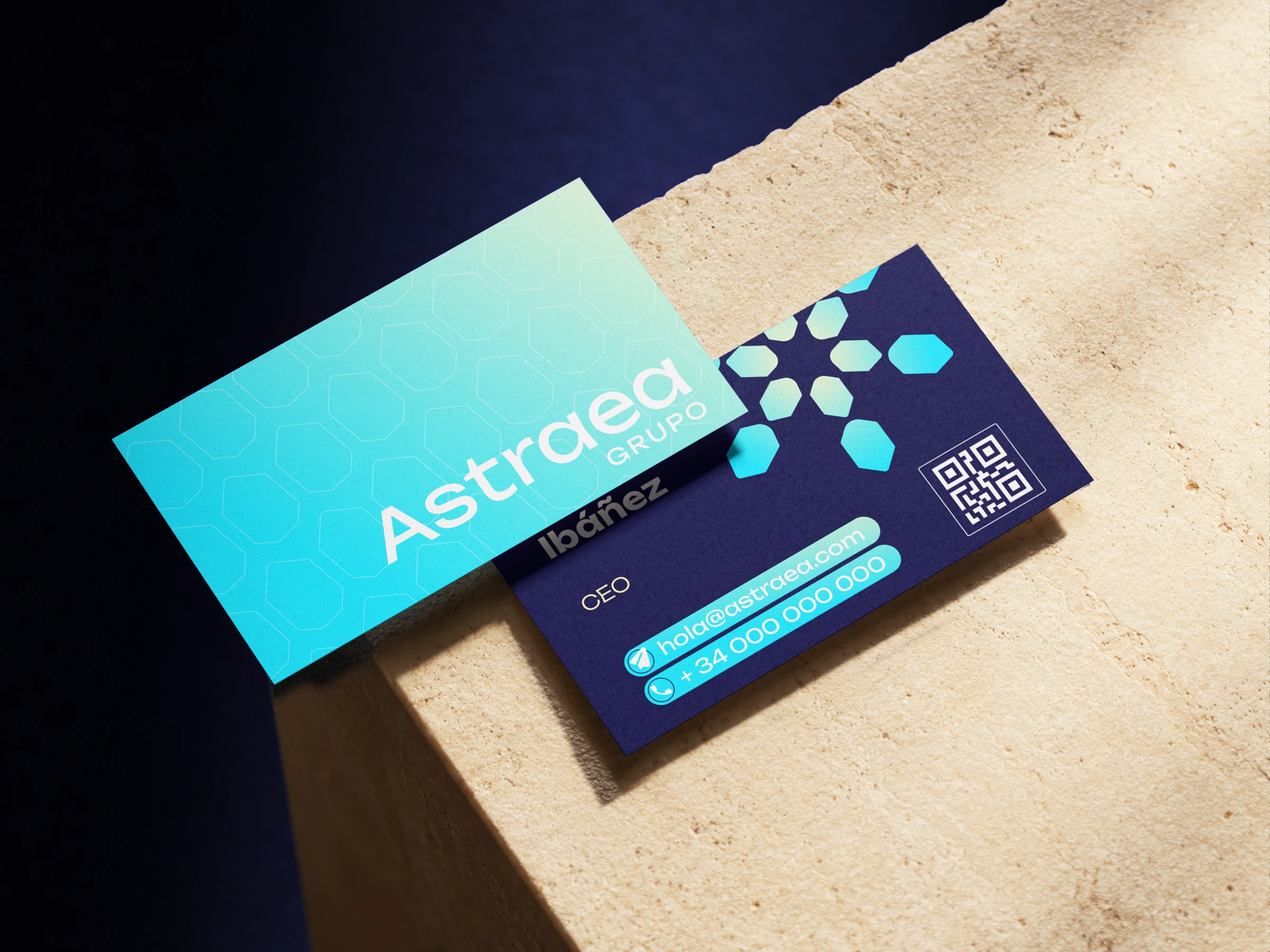 Tarjetas de visita de Astraea Grupo, una turquesa con hexágonos y otra azul marino con el isotipo y un código QR, sobre un bloque de piedra